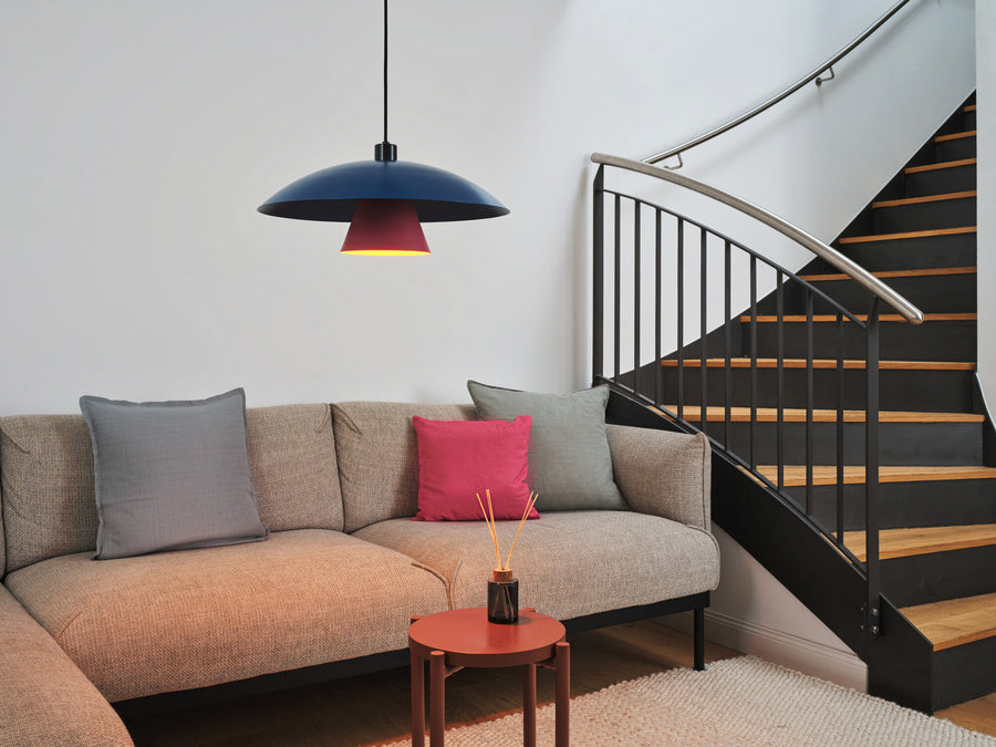 Suspension allumée au-dessus d'un canapé beige, près d'un escalier en intérieur.