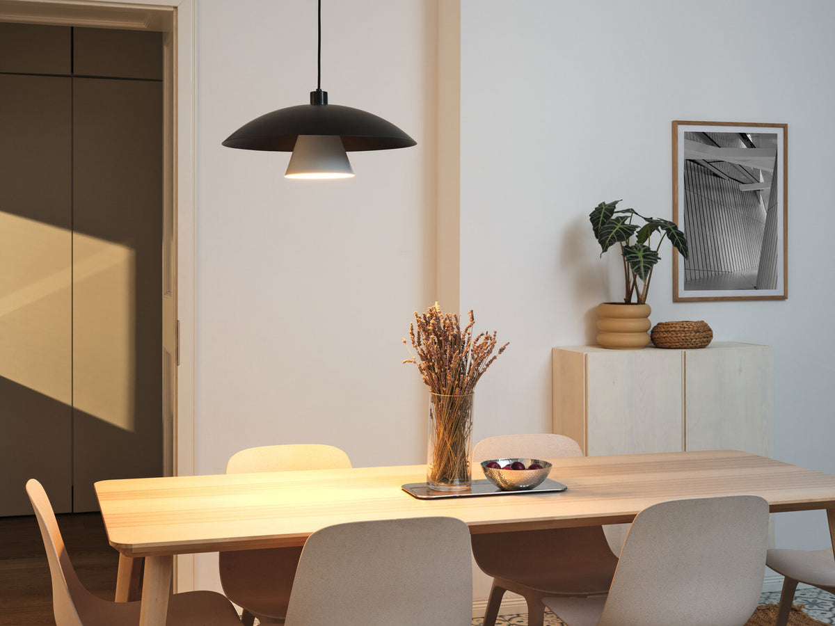 Suspension allumée au-dessus d’une table à manger en bois, intérieur clair.