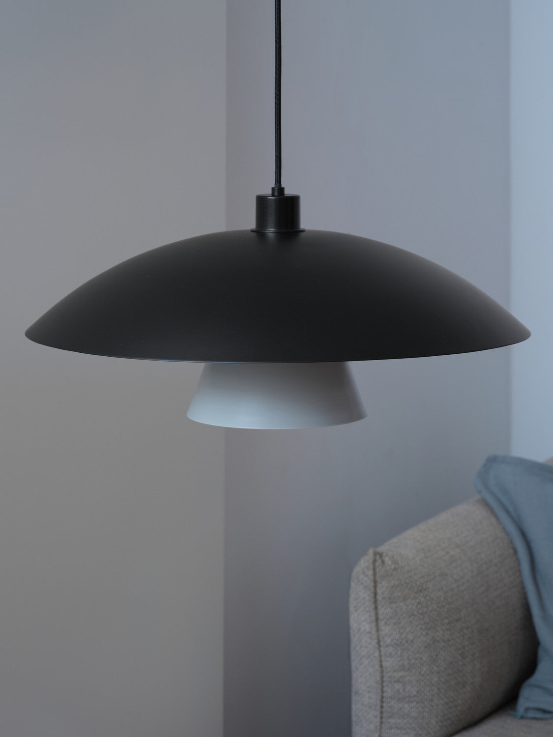 Gros plan sur la suspension noire et blanche devant un mur gris, près d’un canapé.