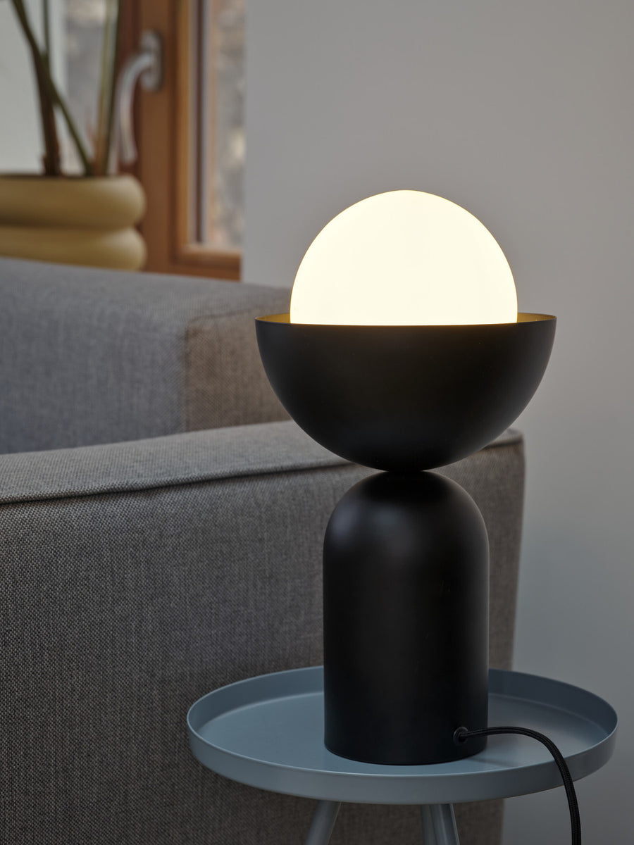 Lampe allumée en gros plan sur une table d'appoint bleue, canapé en fond.