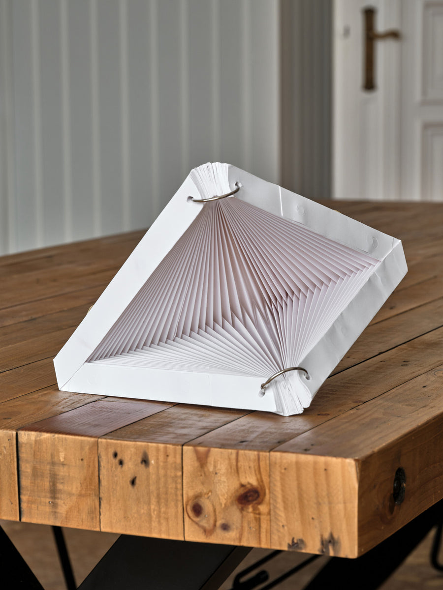 Lanterne dépliée posée sur table en bois, armature métallique et papier plissé apparents