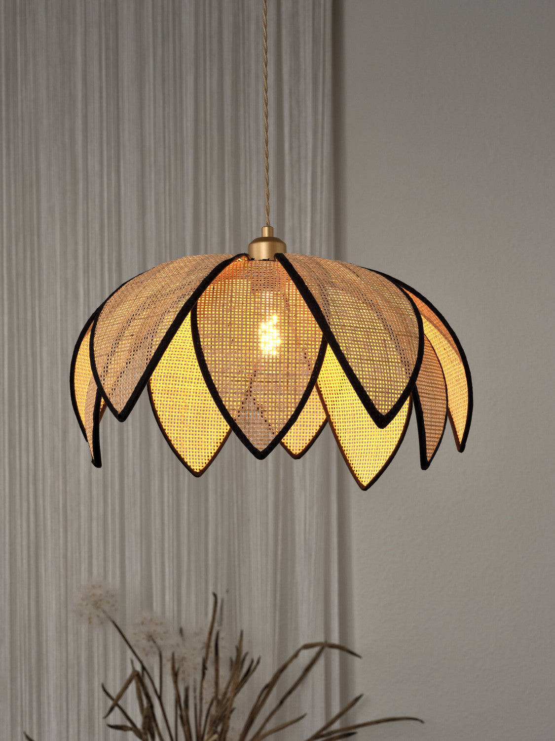 Détail de l’abat-jour lotus éclairé, lumière chaude à travers le cannage tressé.