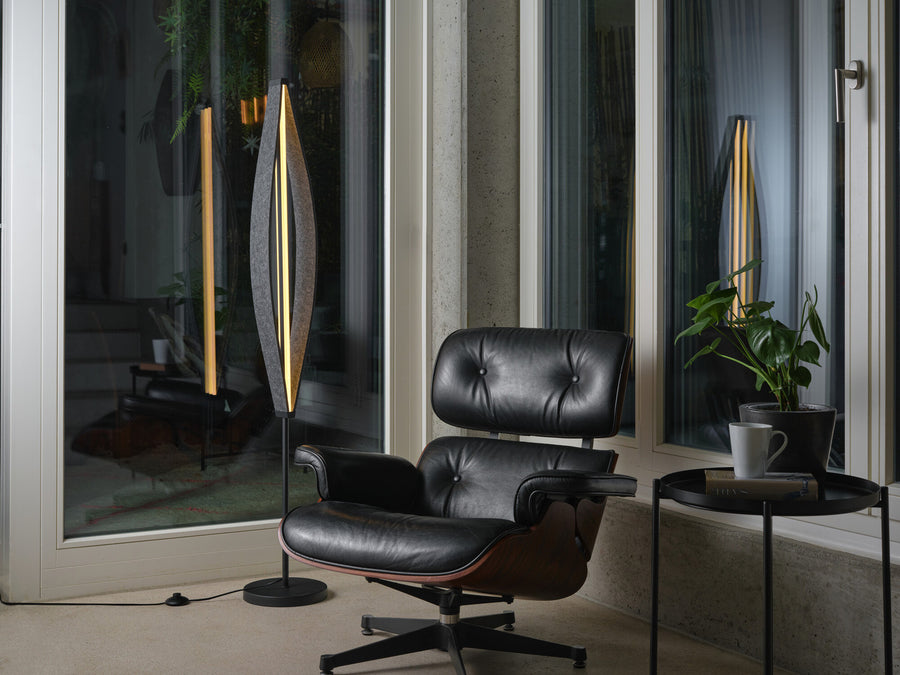 Lampadaire allumé dans un salon contemporain, près d’un fauteuil en cuir noir et d’une plante.