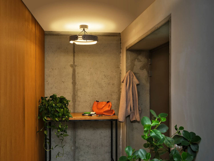 Plafonnier allumé dans une entrée au mur en béton brut.