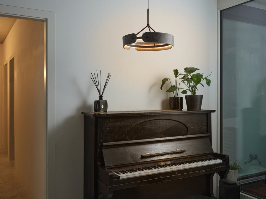 Suspension allumée au-dessus d'un piano noir dans un intérieur chaleureux.