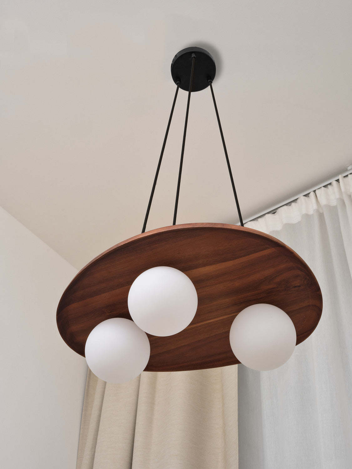 Gros plan sur la suspension en bois et ses trois globes, avec un rideau en arrière-plan.