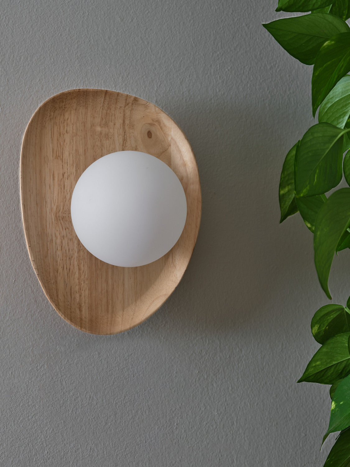 Détail rapproché de la finition bois et du globe opalin sur mur gris