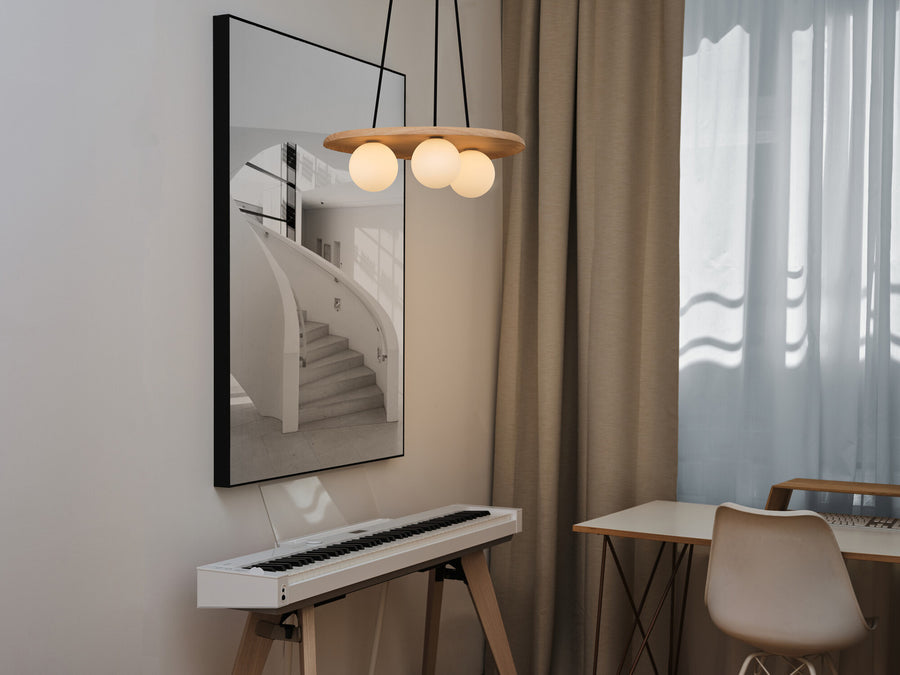 Suspension allumée au-dessus d’un piano dans un intérieur clair et moderne.