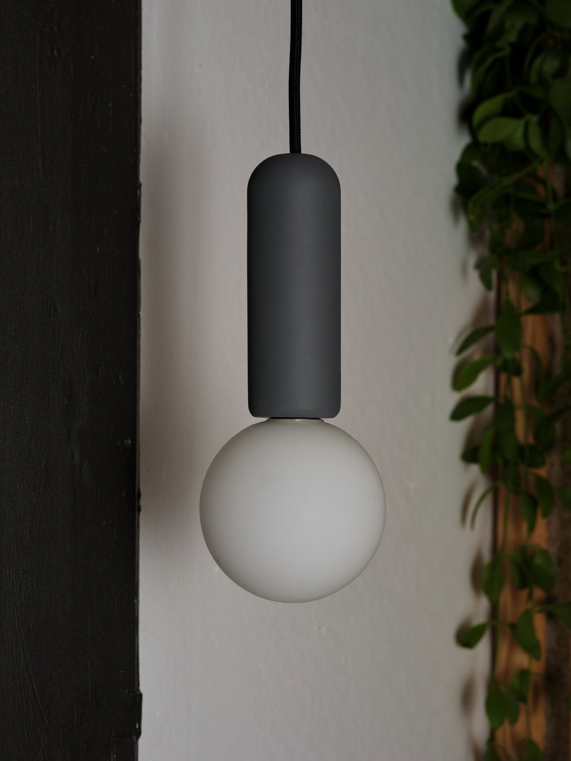 Détail rapproché du cylindre béton anthracite et du globe blanc allumé.