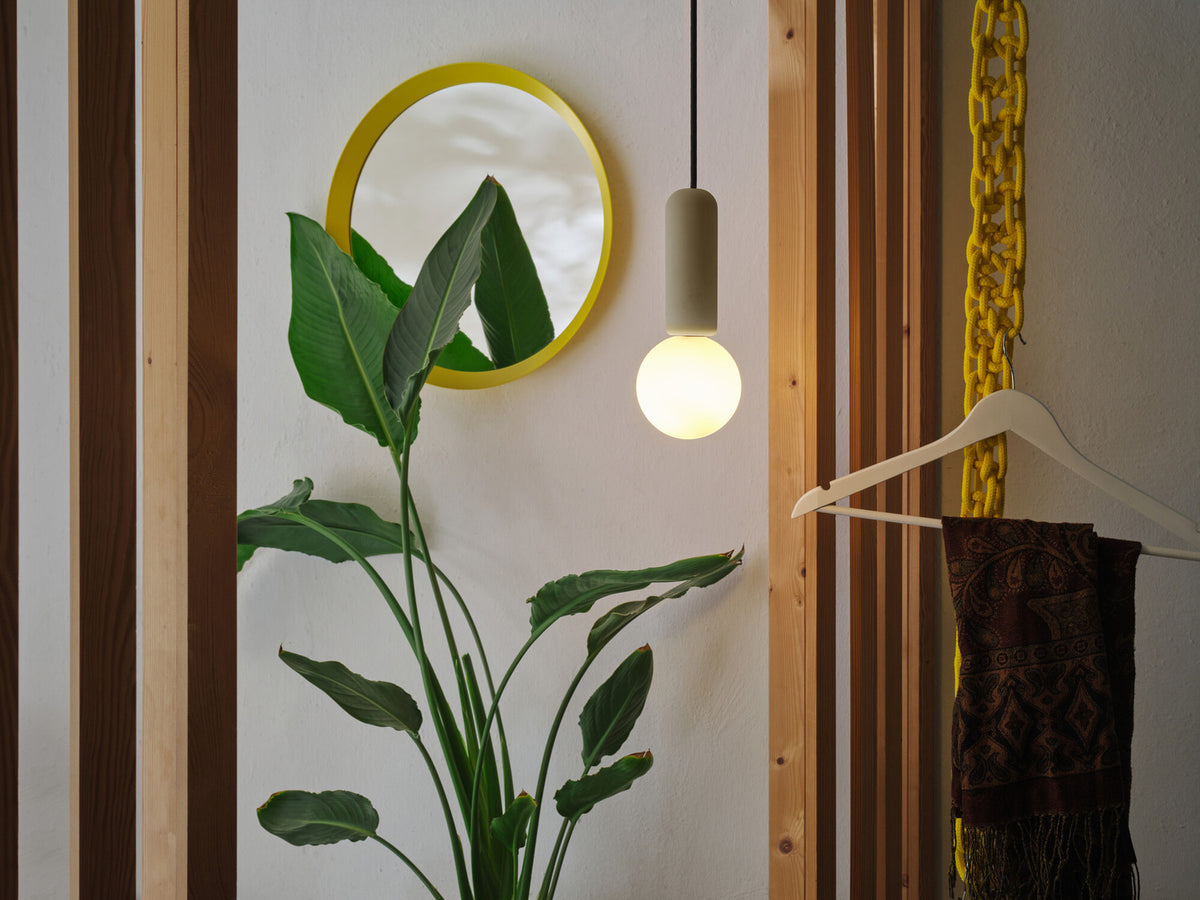 Mise en ambiance dans une entrée avec miroir jaune, plante et suspension allumée.