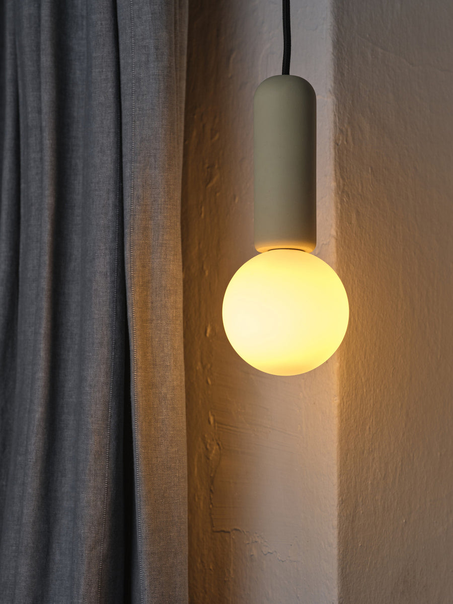 Suspension allumée près d'un mur texturé et d'un rideau gris, lumière chaude.