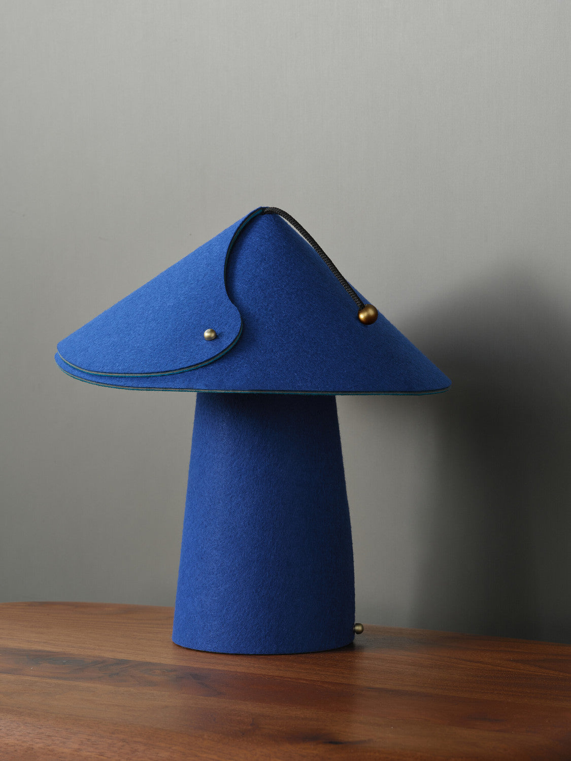 Lampe bleue vue de face, abat-jour en feutre replié et fermeture à glissière apparente.
