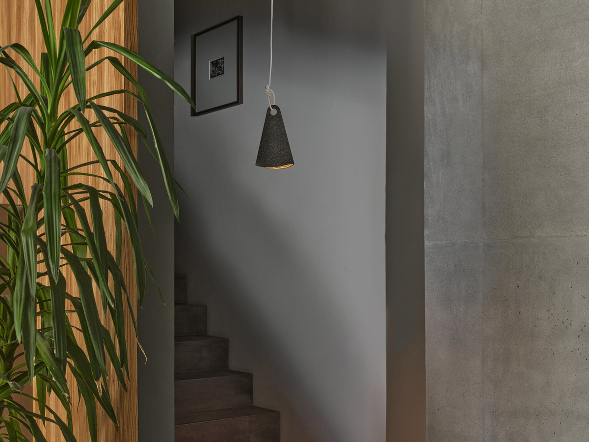 Mise en ambiance dans un escalier sombre, suspension noire éclairée au-dessus des marches.