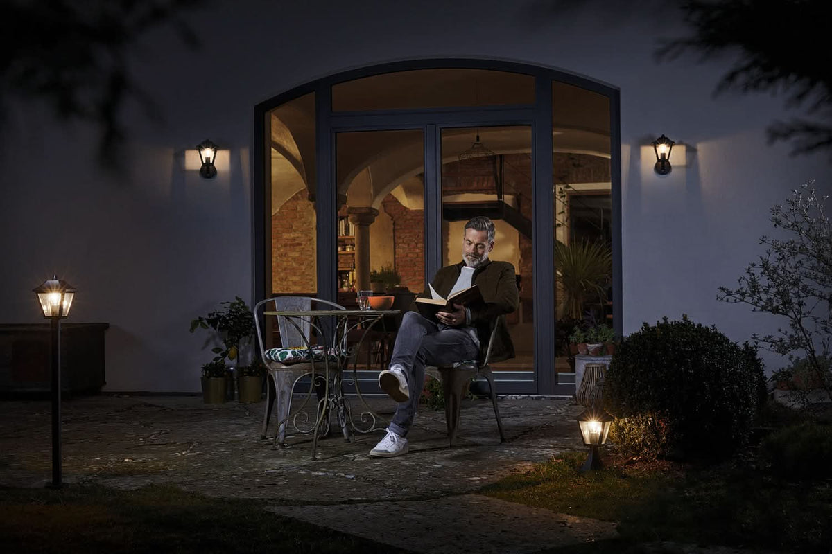 Homme lisant sur terrasse de nuit, deux appliques murales éclairent une grande baie vitrée.