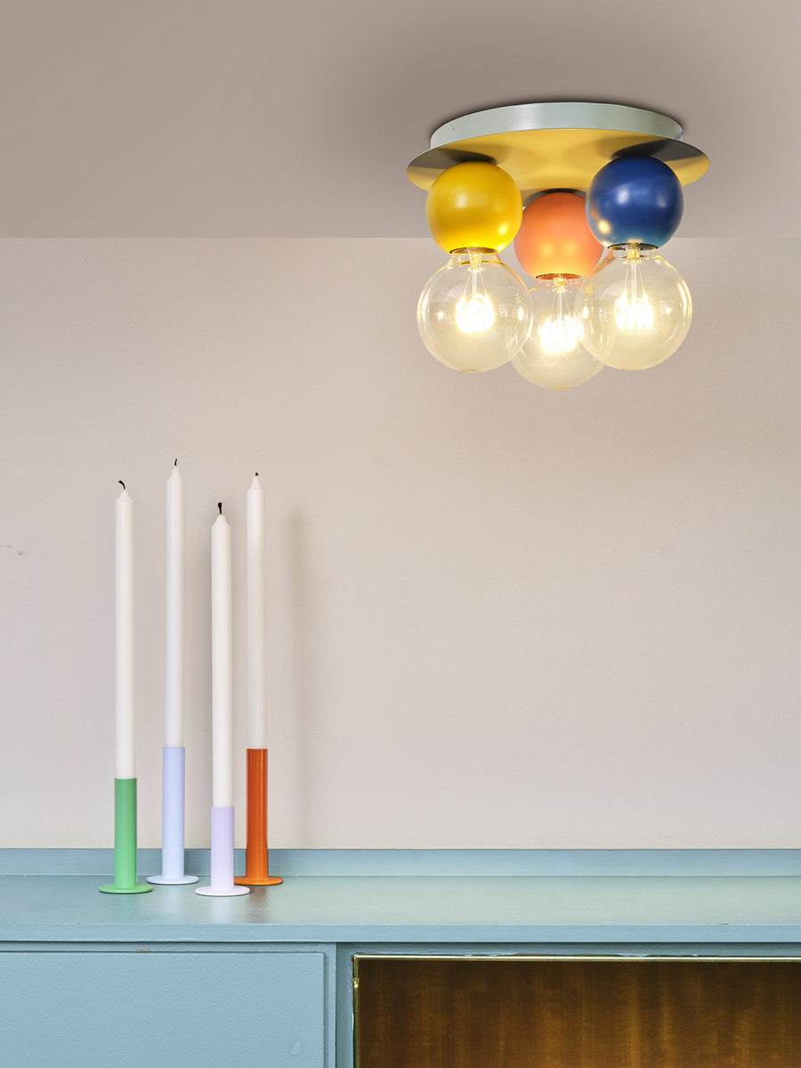 Gros plan du plafonnier allumé, globes colorés et ampoules visibles au-dessus du meuble.