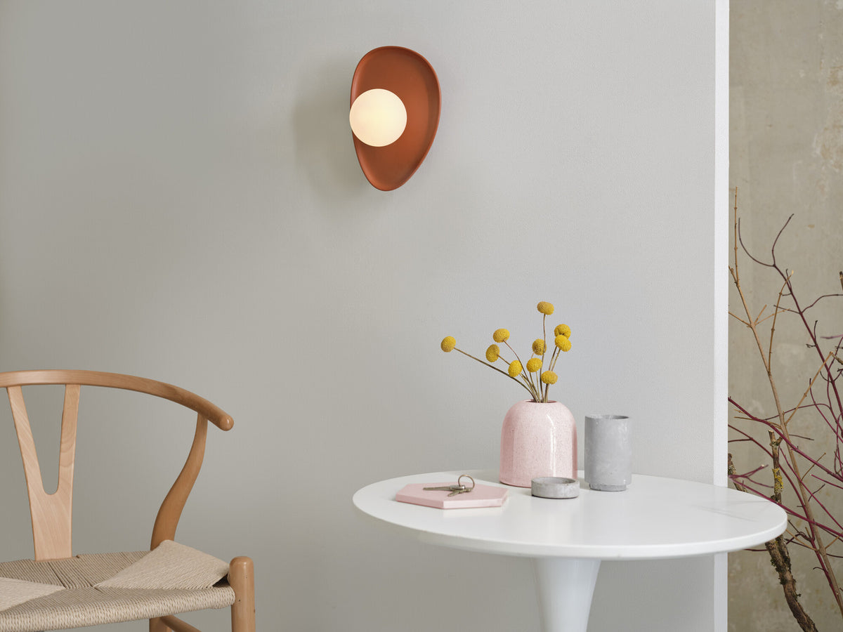 Applique murale brune fixée sur un mur clair au-dessus d’une table avec fleurs jaunes.
