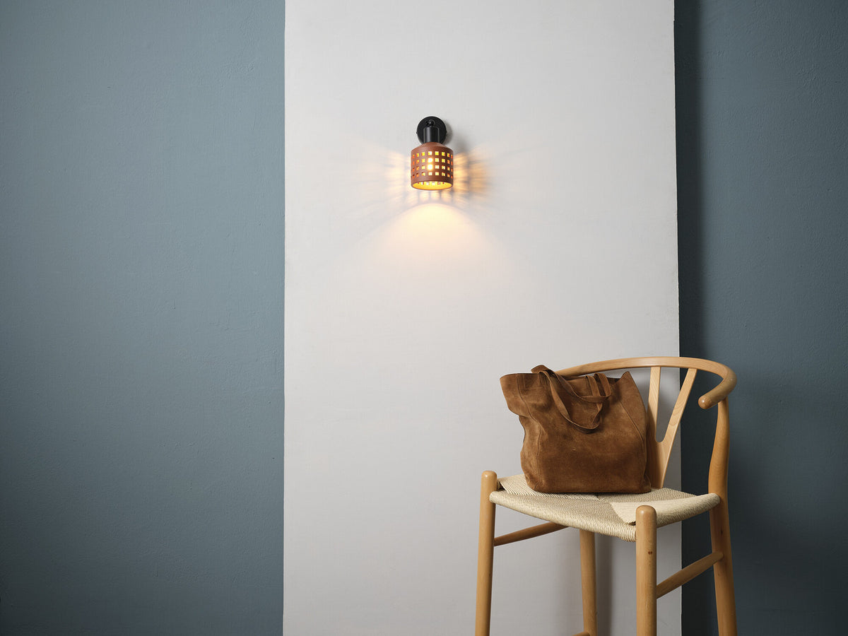 Applique murale allumée sur mur blanc, ombres projetées, chaise en bois et sac.