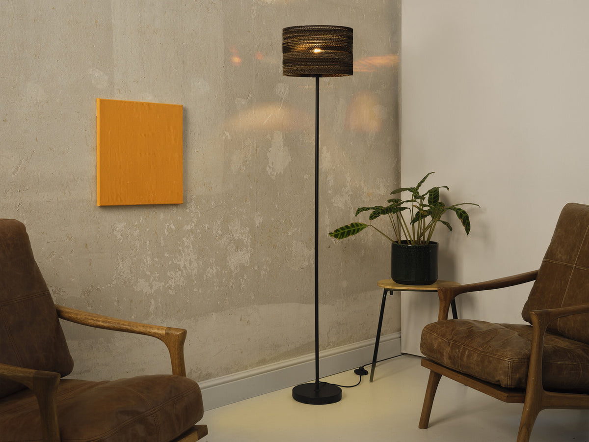 Mise en ambiance dans un salon, lampadaire allumé entre deux fauteuils en cuir.