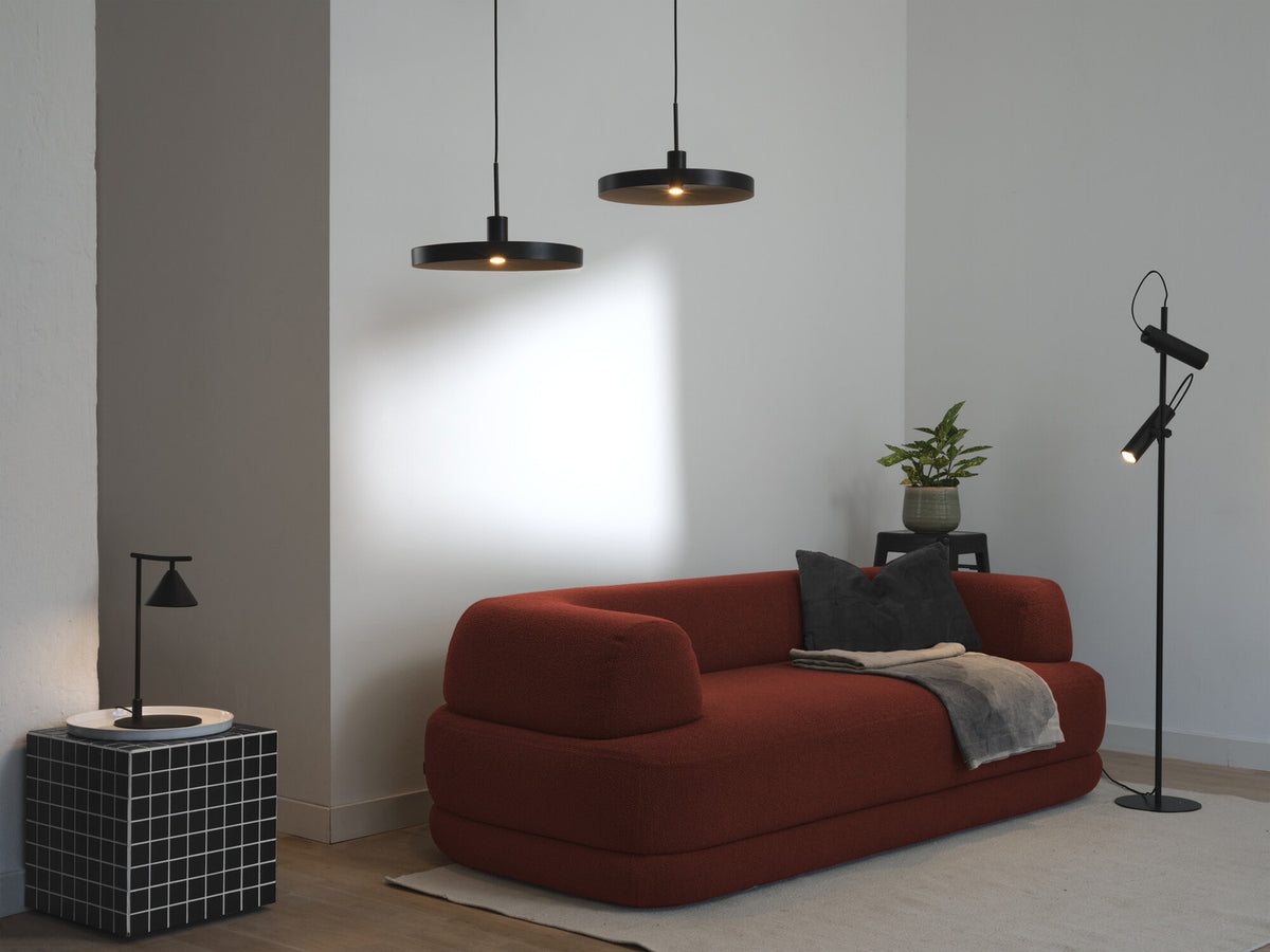 Lampadaire noir en situation dans un salon meublé d'un canapé rouge.