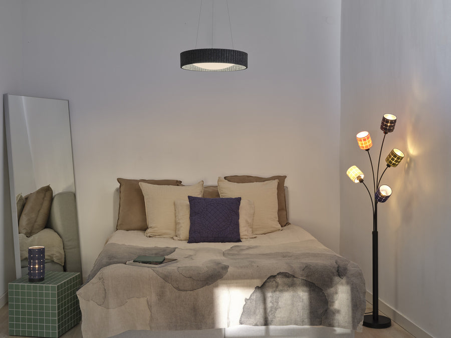 Lampadaire à cinq abat-jours colorés allumé dans une chambre, près d'un lit et d'un miroir.