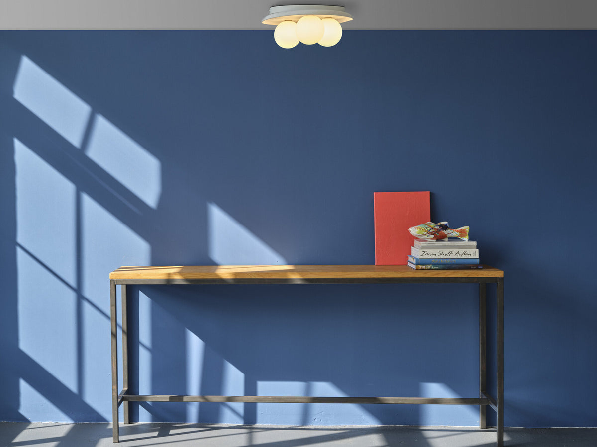 Mise en ambiance sur mur bleu profond, plafonnier allumé au-dessus d'une console en bois