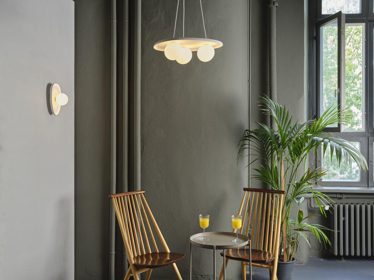 Scène d'intérieur avec suspension ovale et applique murale allumées, fauteuils et plante