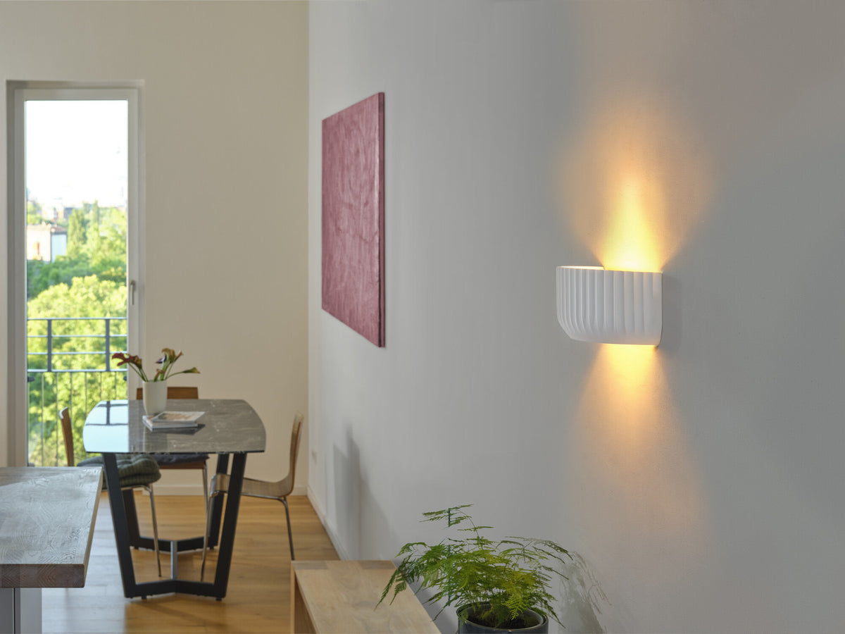 Mise en ambiance dans une salle à manger, applique allumée diffusant une lumière chaude.