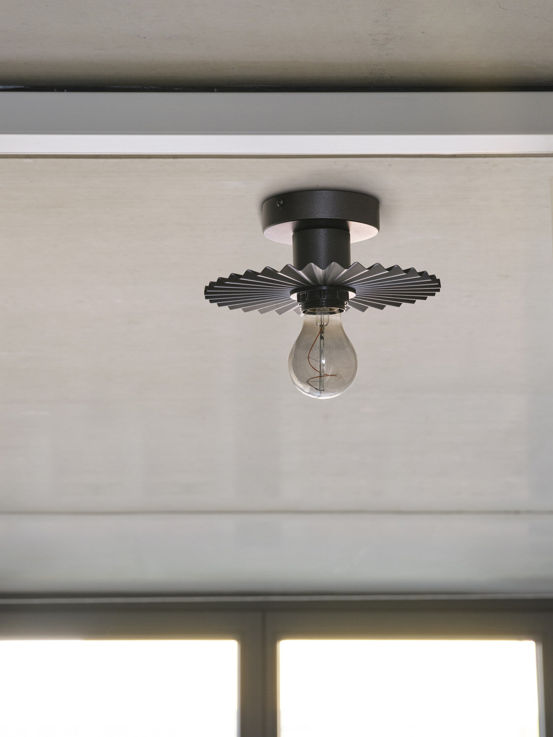 Plafonnier anthracite monté au plafond, ampoule transparente éteinte, vue de dessous.