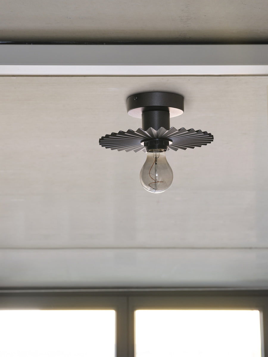 Plafonnier anthracite monté au plafond, ampoule transparente éteinte, vue de dessous.