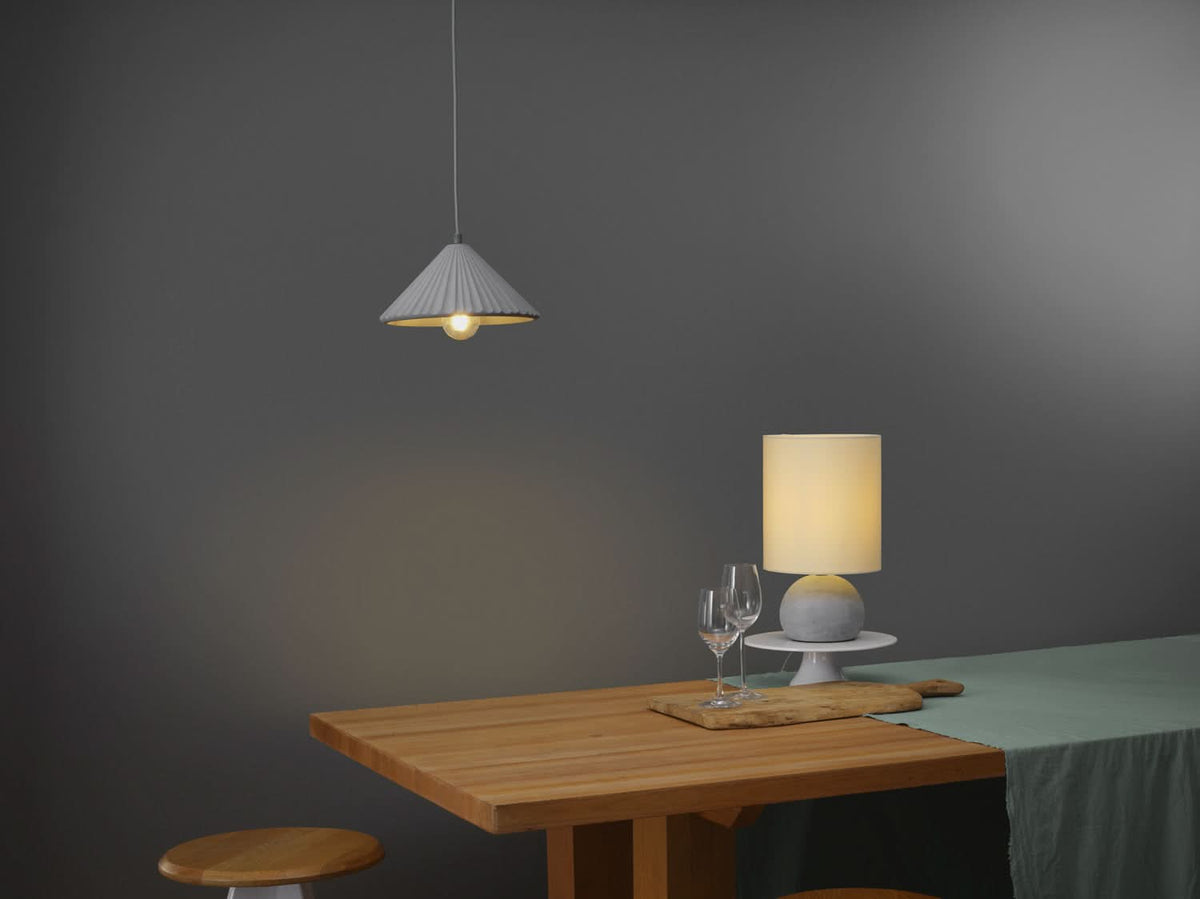 Salle à manger sombre avec lampe de table allumée et suspension conique au-dessus.