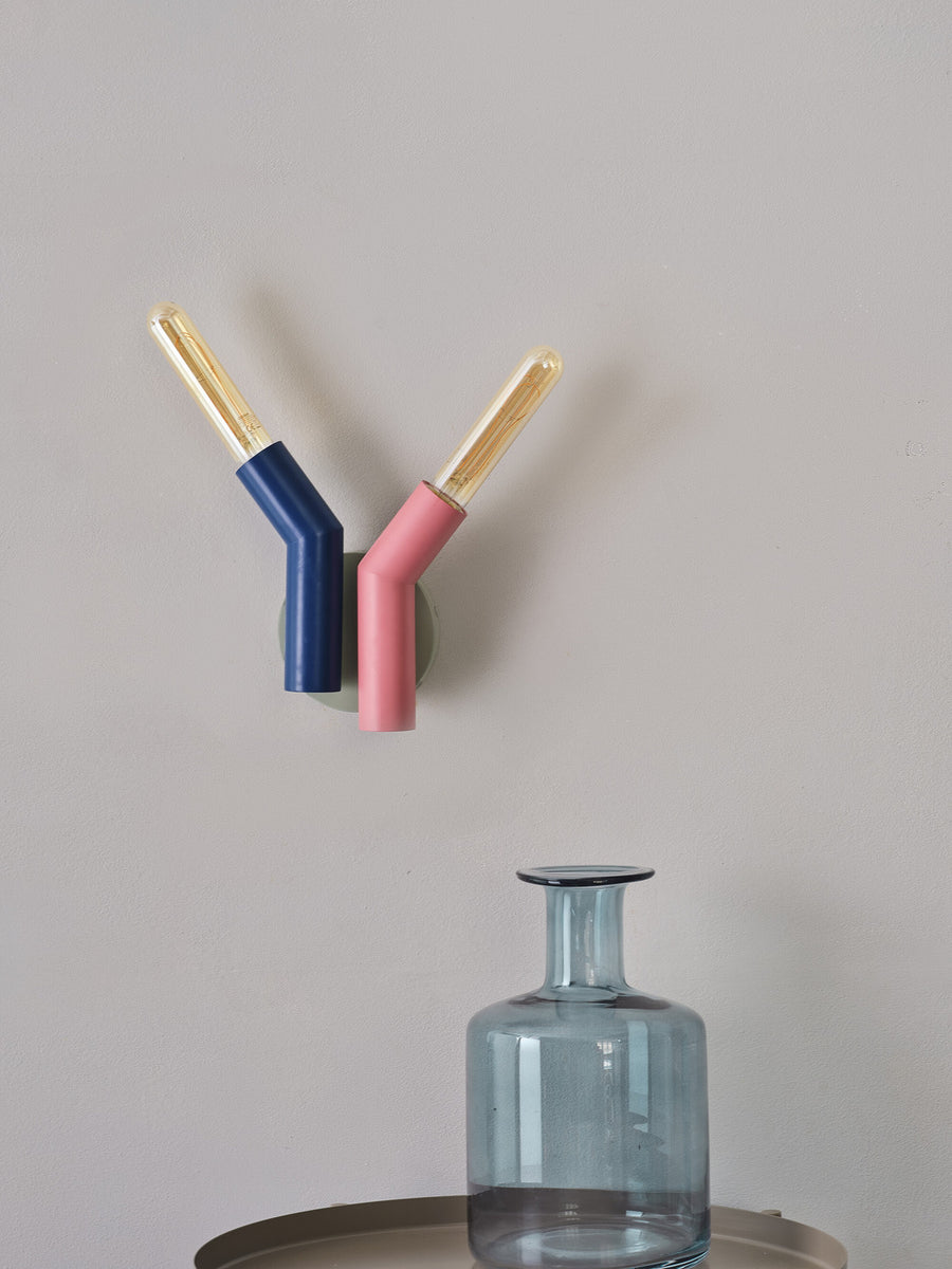 Luminaire mural à deux bras inclinés au-dessus d'un vase en verre bleu.