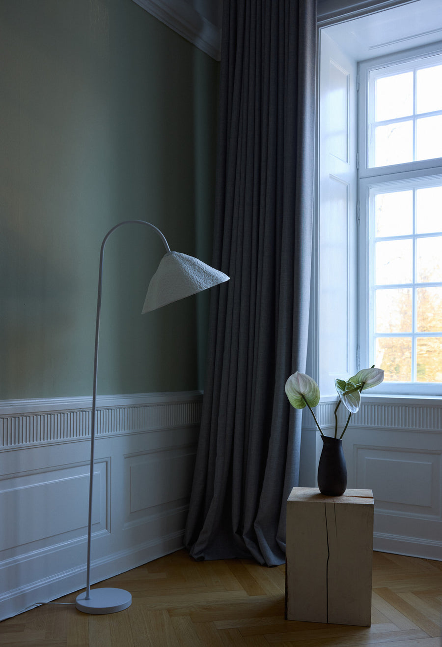 Lampadaire allumé dans un salon classique aux murs verts avec moulures et rideaux.