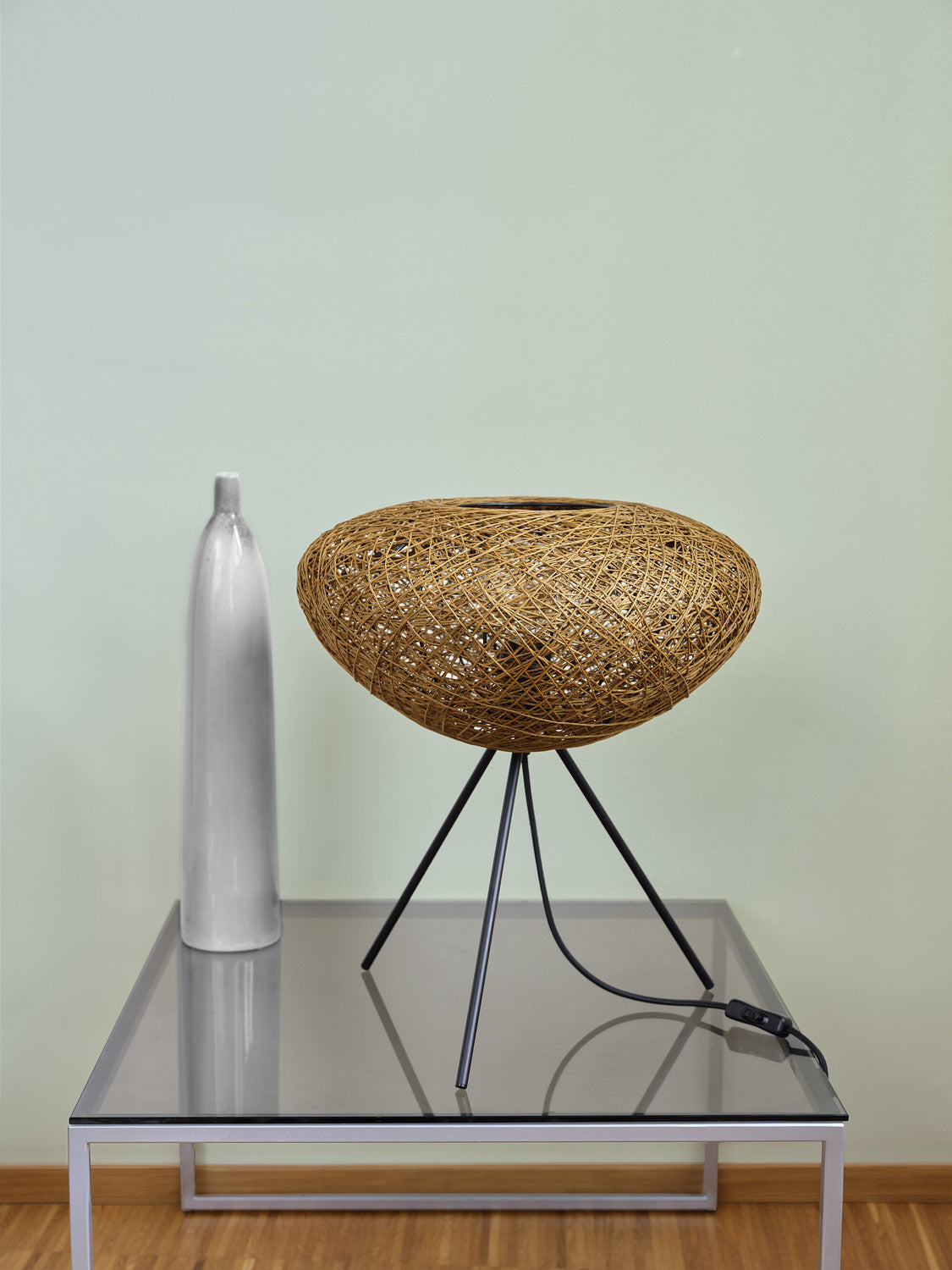 Lampe éteinte sur table en verre aux côtés d'un vase blanc élancé.