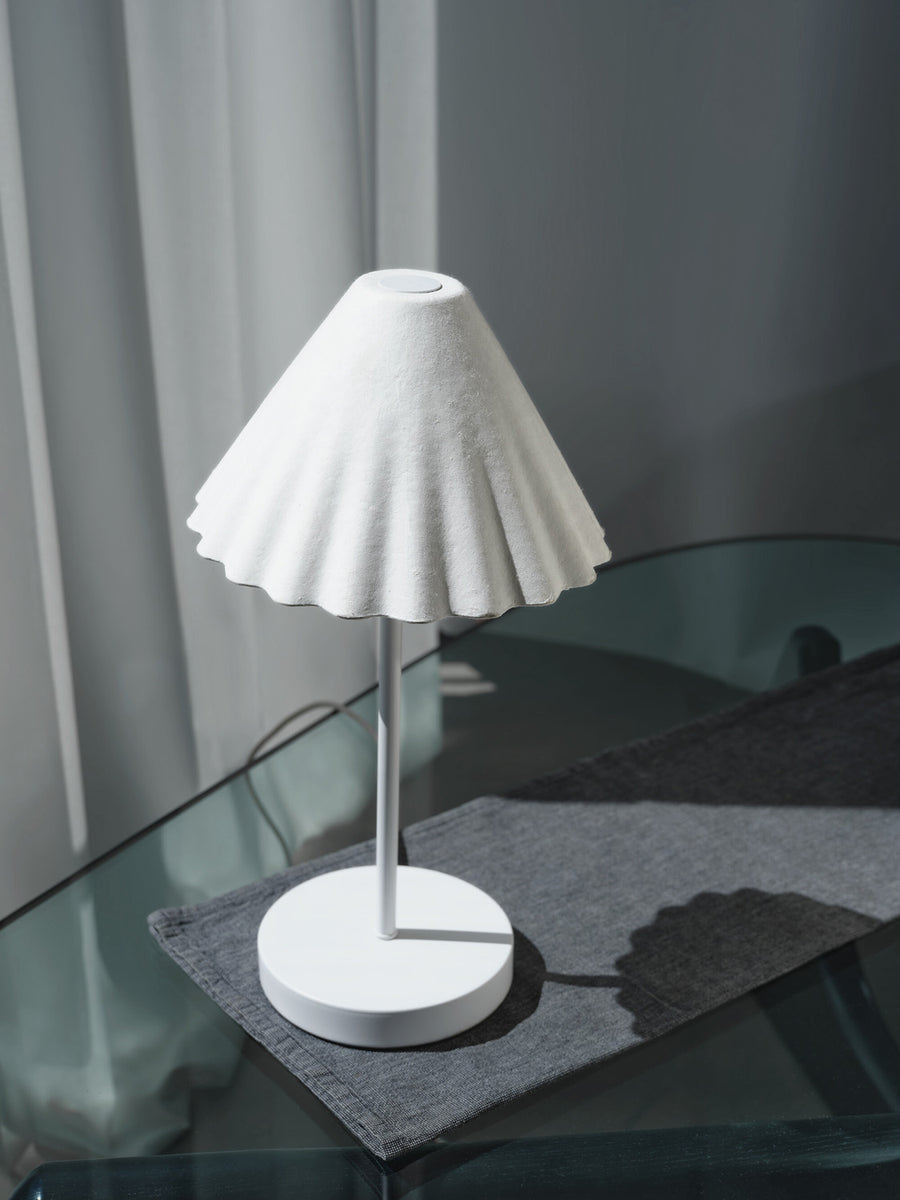 Vue rapprochée de la lampe blanche sur set gris, abat-jour plissé et finition mate.