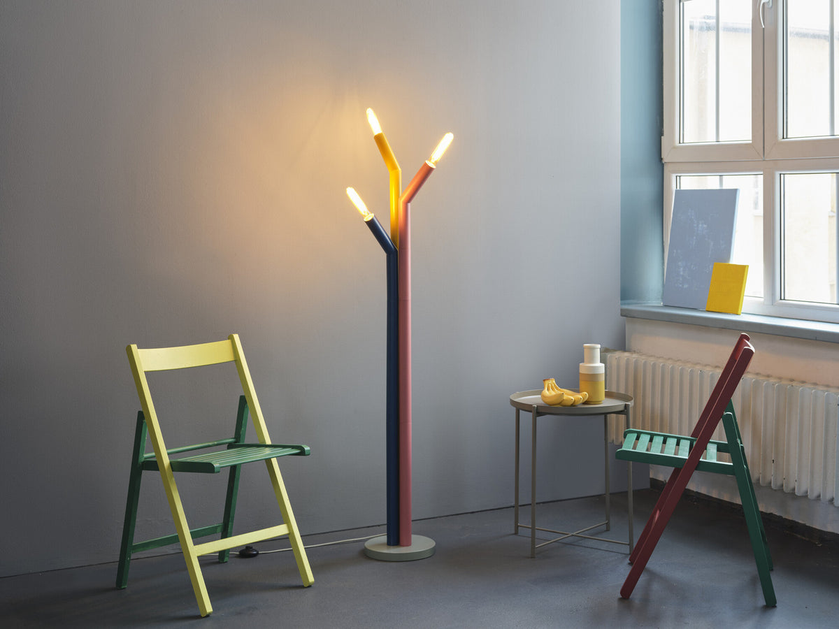 Lampadaire allumé dans un salon gris, entouré de chaises pliantes colorées et petite table.