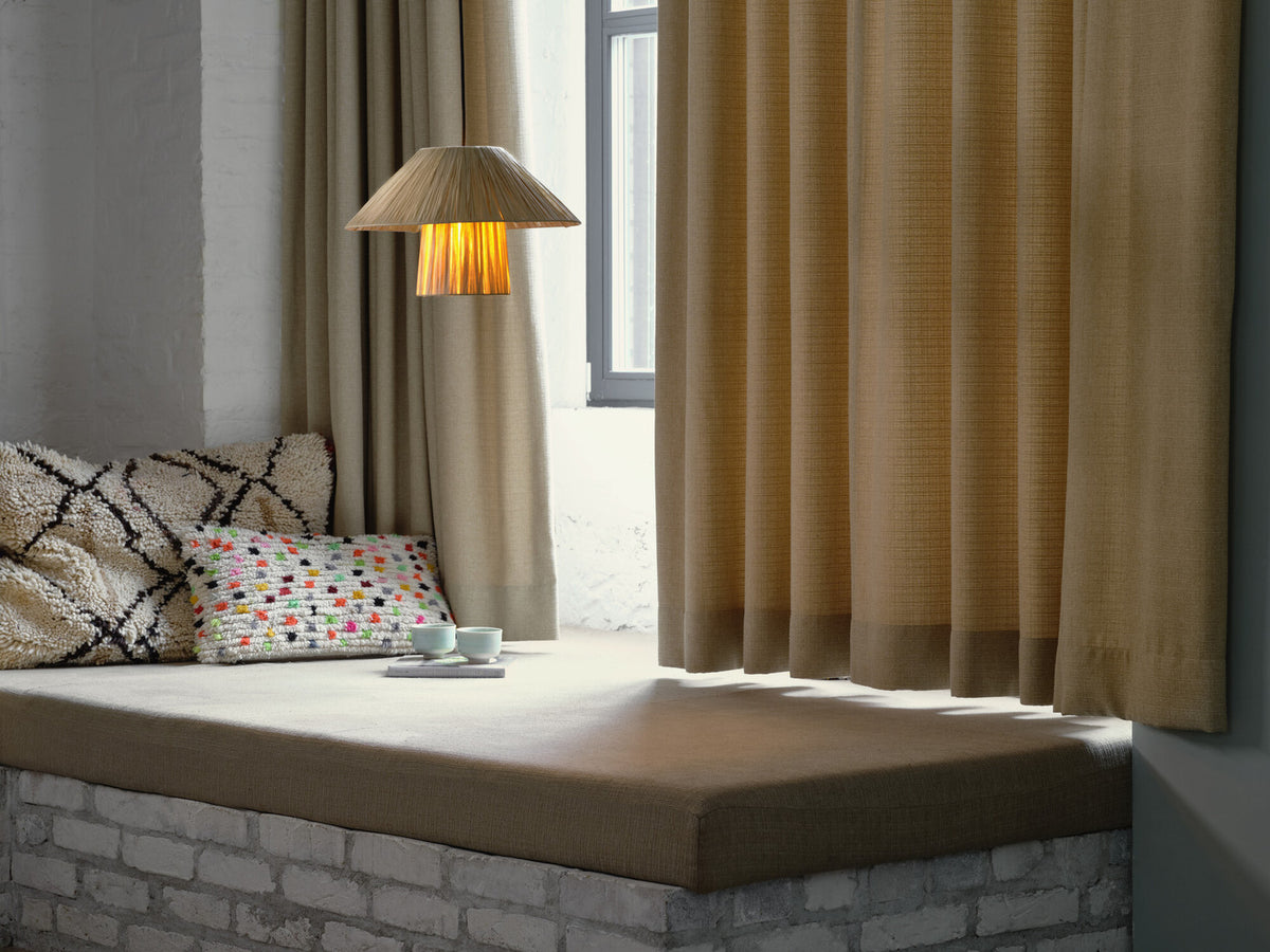 Détail de la suspension allumée au-dessus d’une banquette, rideaux et coussins colorés.