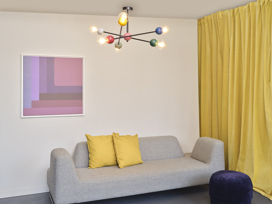 Suspension allumée au-dessus d'un canapé gris, coussins jaunes et rideau assorti.