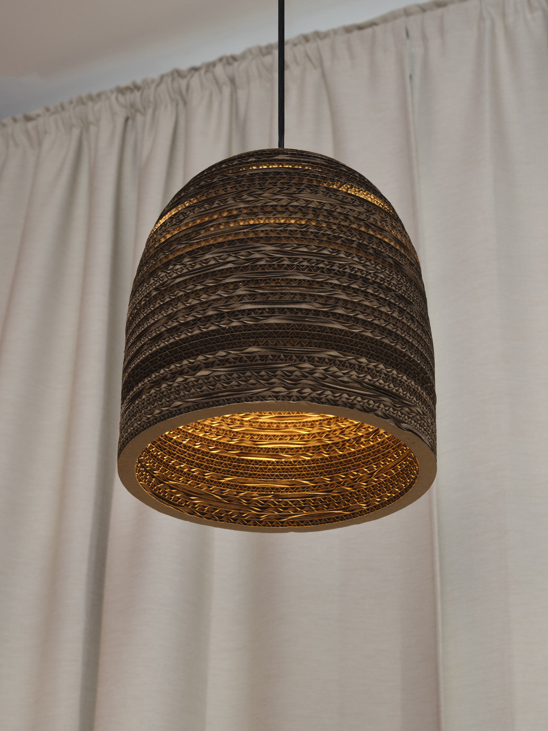 Détail rapproché de l'abat-jour allumé, lumière chaude sur fond de rideau clair.