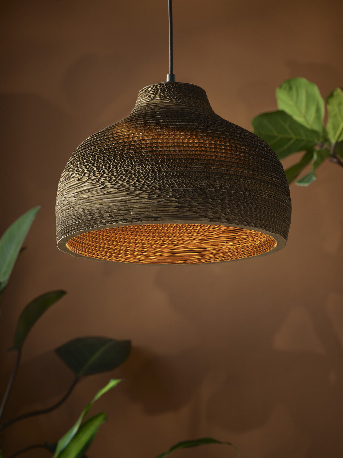 Gros plan sur l'abat-jour en carton allumé, révélant le motif tissé et la lumière chaude.