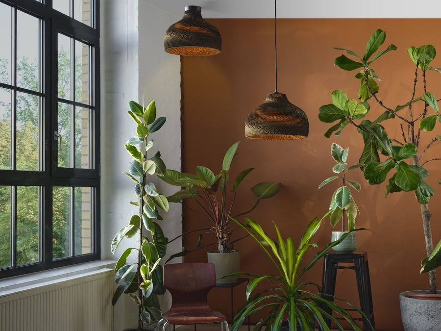 Deux suspensions en carton dans une pièce avec plantes, chaise et grande fenêtre lumineuse.