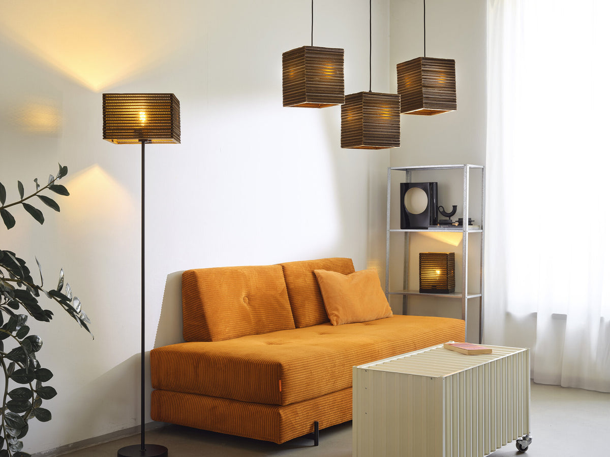 Ambiance salon avec suspensions en carton, lampadaire et meuble, éclairage chaleureux.