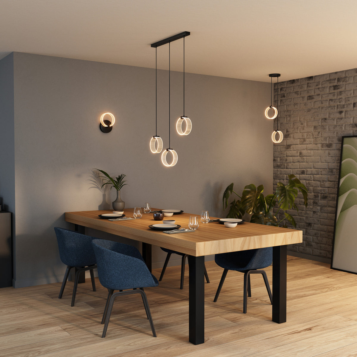 Repas dressé sous lumière chaude, suspension à trois anneaux au-dessus de la table en bois.