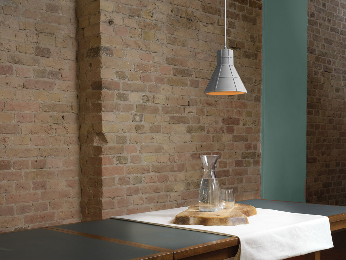 Suspension en béton éclairée au-dessus d'une table dressée devant un mur de briques.