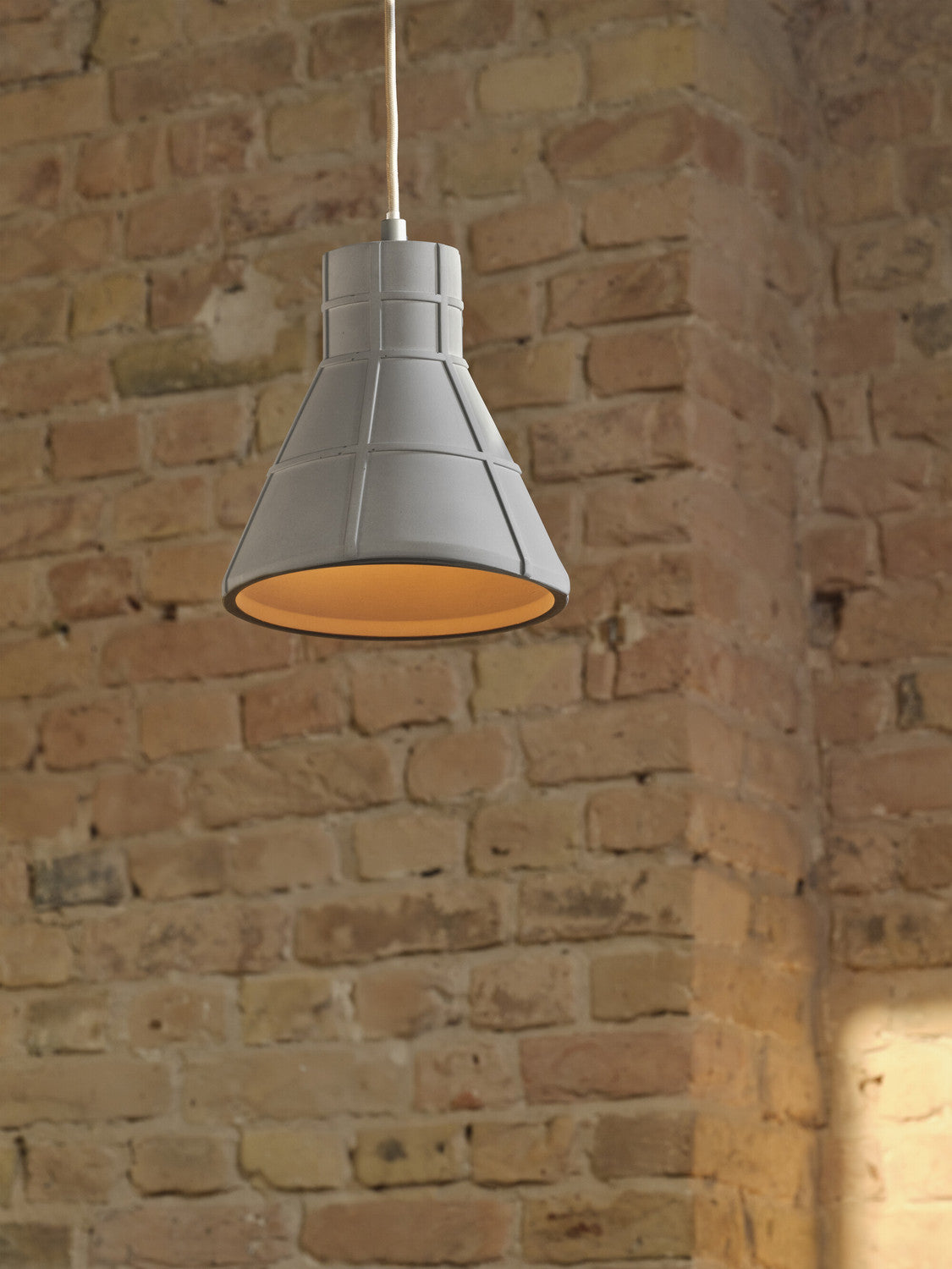 Gros plan sur l'abat-jour en béton et son intérieur doré, devant un mur de briques.
