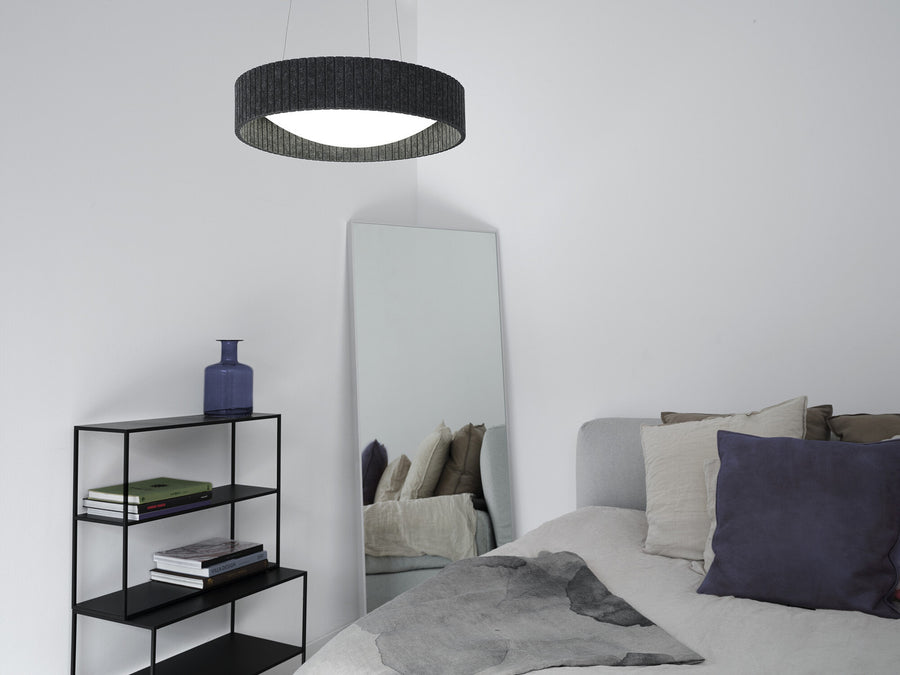 Suspension cylindrique allumée dans une chambre, près d’un miroir et d’une étagère.