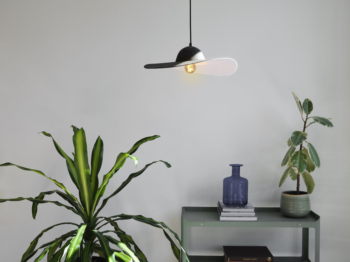 Suspension en feutre allumée au-dessus d'une console verte avec végétaux et vase.