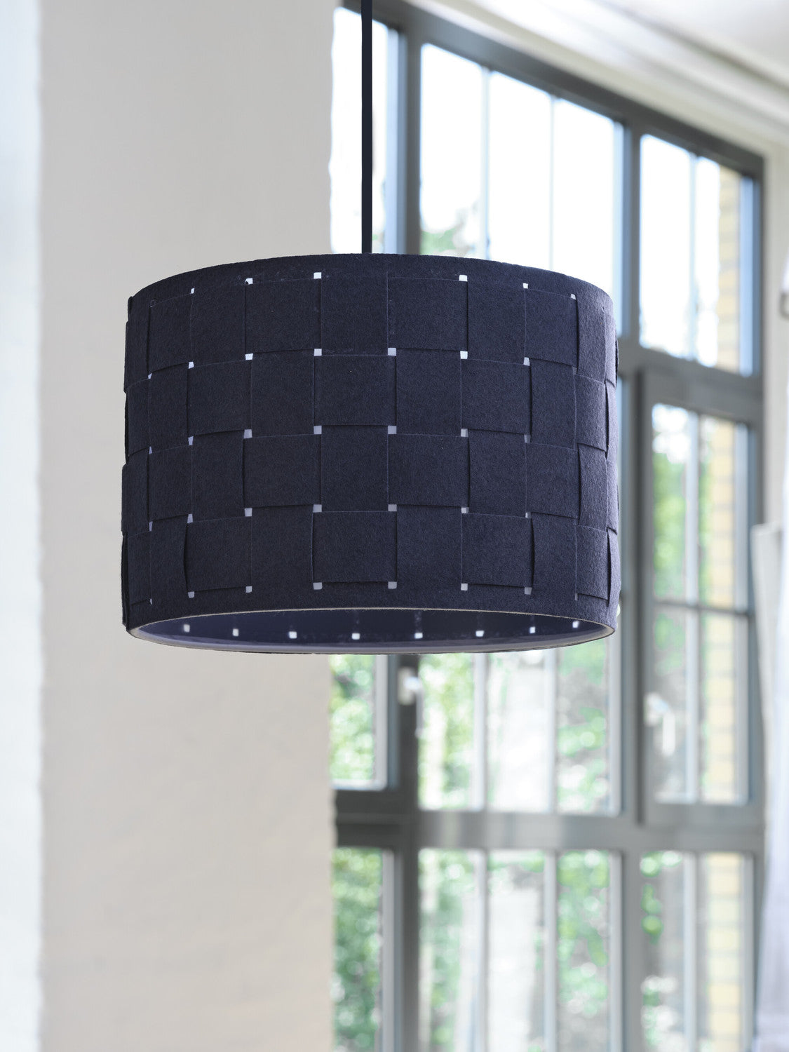 Suspension anthracite devant une fenêtre, lumière du jour traversant le feutre tissé.