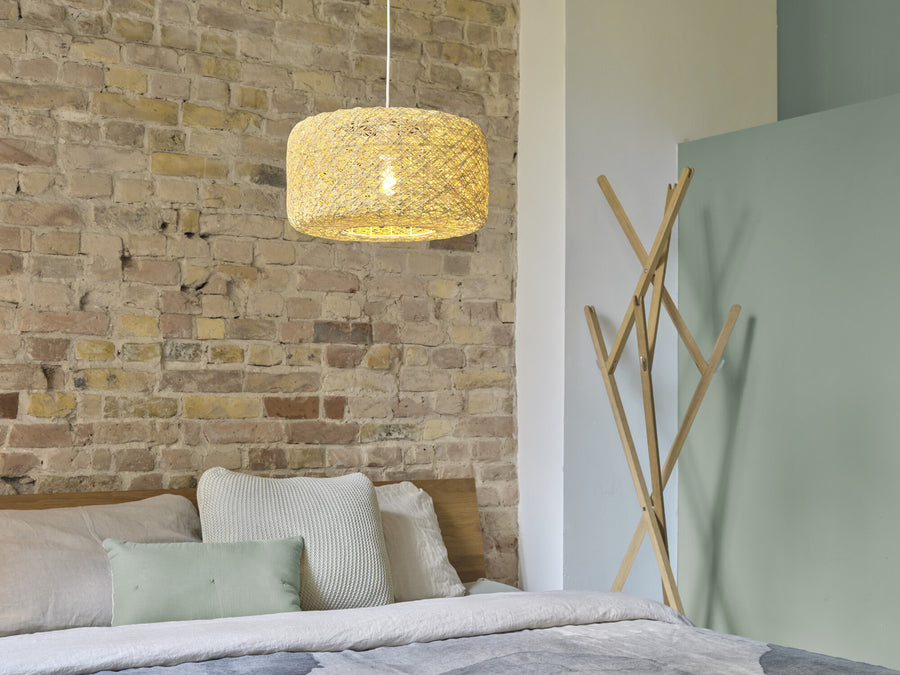 Suspension beige suspendue devant un mur en briques, dans une chambre.