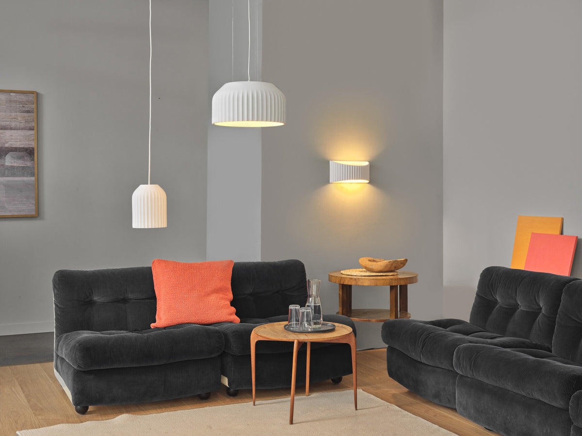 Suspension blanche au-dessus d'un canapé noir, dans un salon gris lumineux