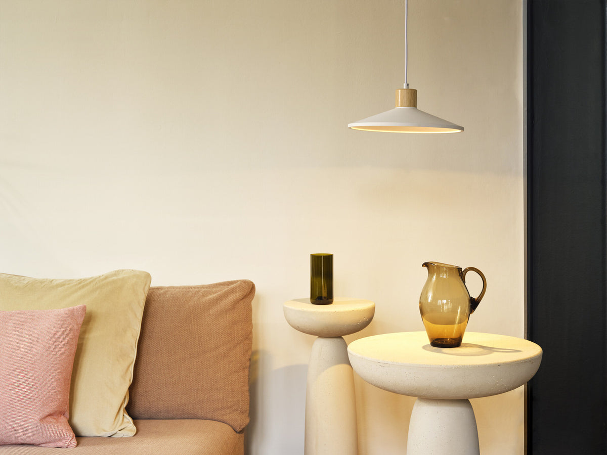 Suspension allumée au-dessus d’un canapé beige, ambiance chaleureuse avec coussins et tables.